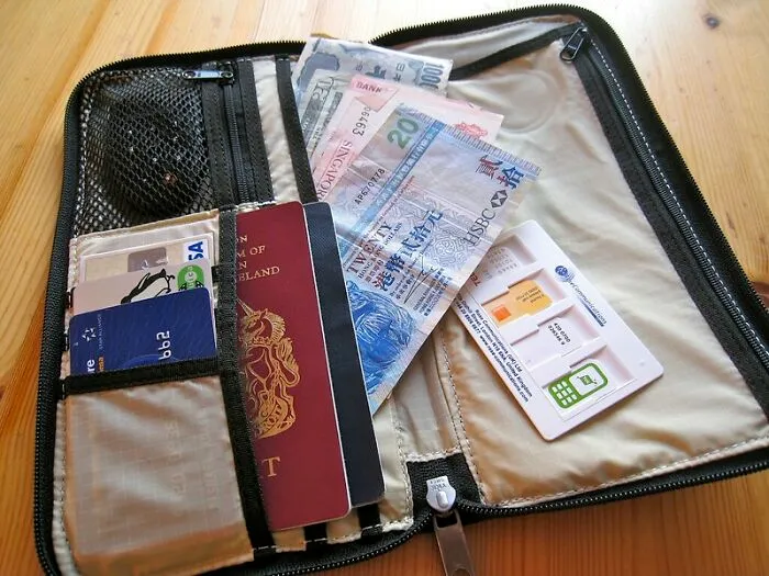 Open travel wallet with various currency notes, passport, and cards highlighting things the poor know but the rich don't.