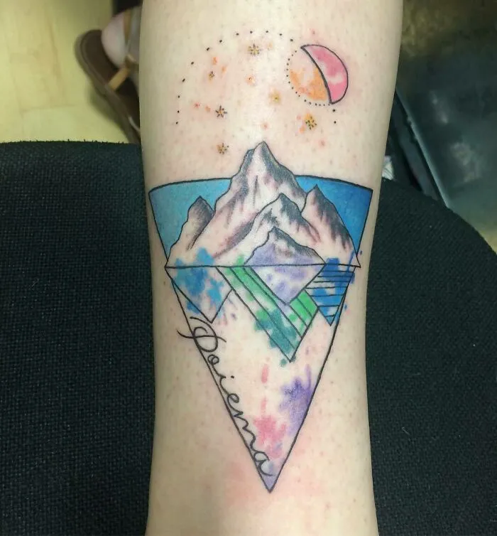 Geometric tattoo design on leg featuring mountains, moon, and abstract shapes in vibrant colors.