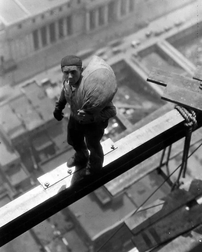 1930. Un obrero fuma un cigarrillo y lleva un bolso al hombro. Hace una pausa en medio de una viga de acero a gran altura sobre las calles de la ciudad, durante la construcción del edificio de la Manhattan Company en el número 40 de Wall Street, Nueva York. Foto de Arthur Gerlach