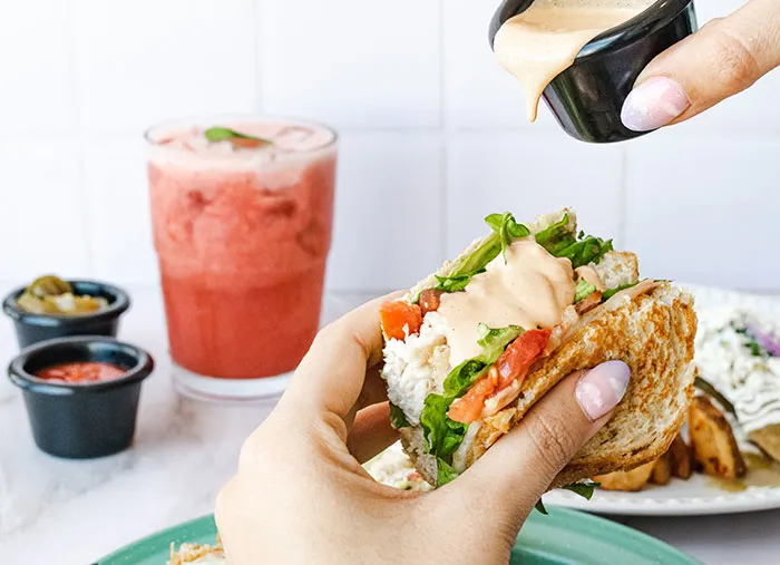 A person pouring dressing on a sandwich