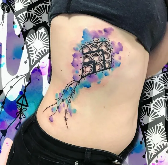 Watercolor tattoo on a person's side featuring a geometric design with blue and purple inkspiration.