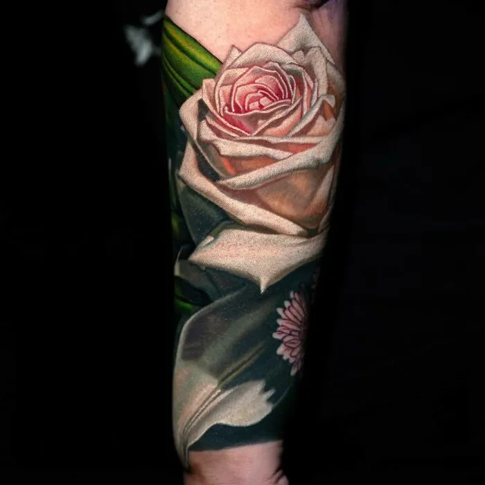 Realistic tattoo of a light pink rose with detailed petals on an arm.