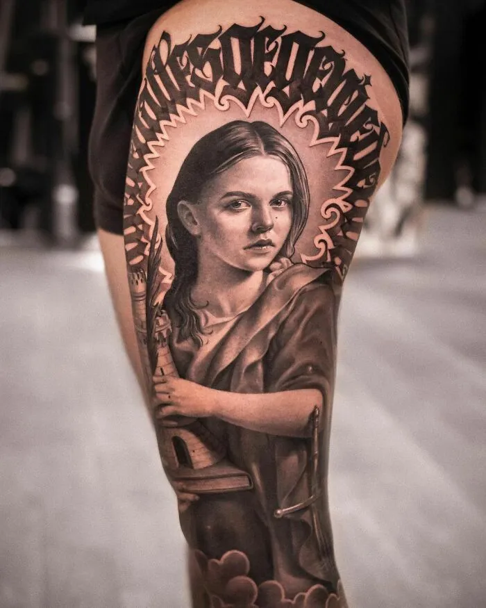 Realistic St. Barbara portrait tattoo on leg, featuring intricate detailing with graffiti art above.