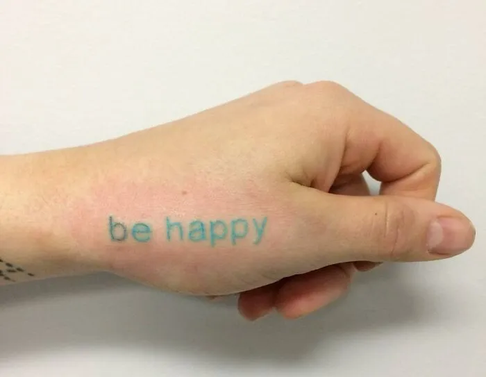 Word tattoo reading "be happy" on a person's hand for inkspiration.