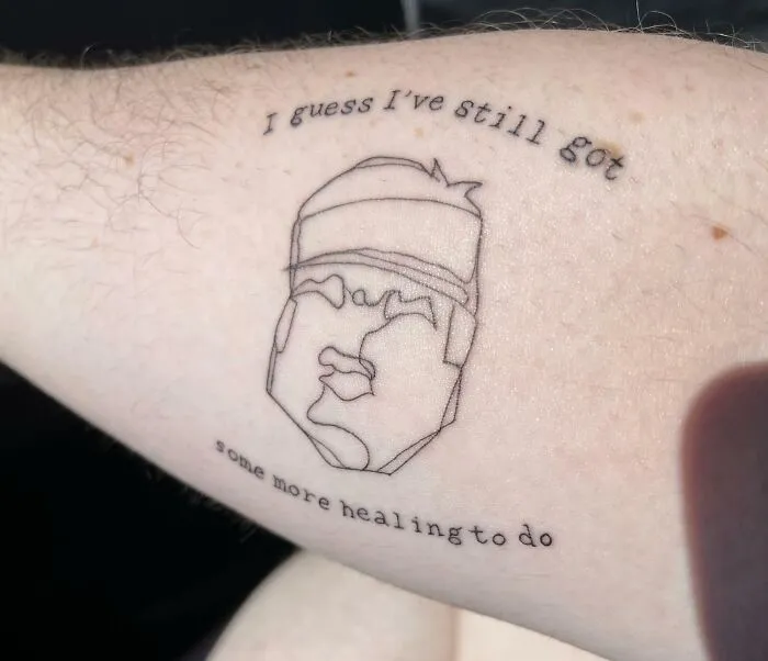 Line art tattoo with text "I guess I've still got some more healing to do" on arm; creative word tattoos.