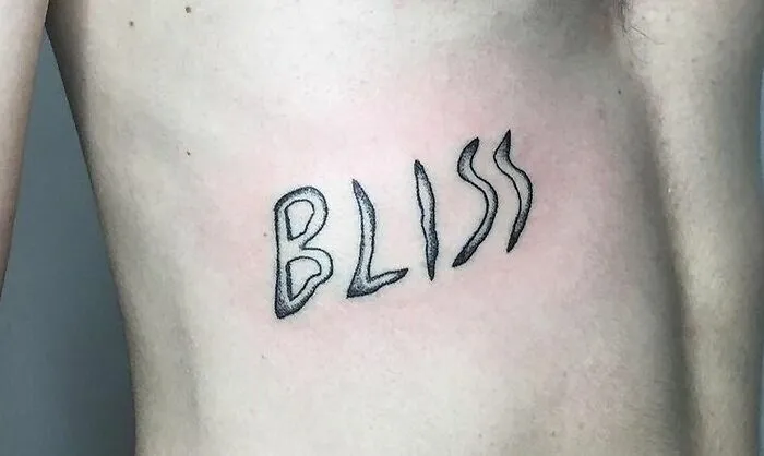"Word tattoo 'BLISS' in unique font on a person's side, showcasing creative tattoo ideas."