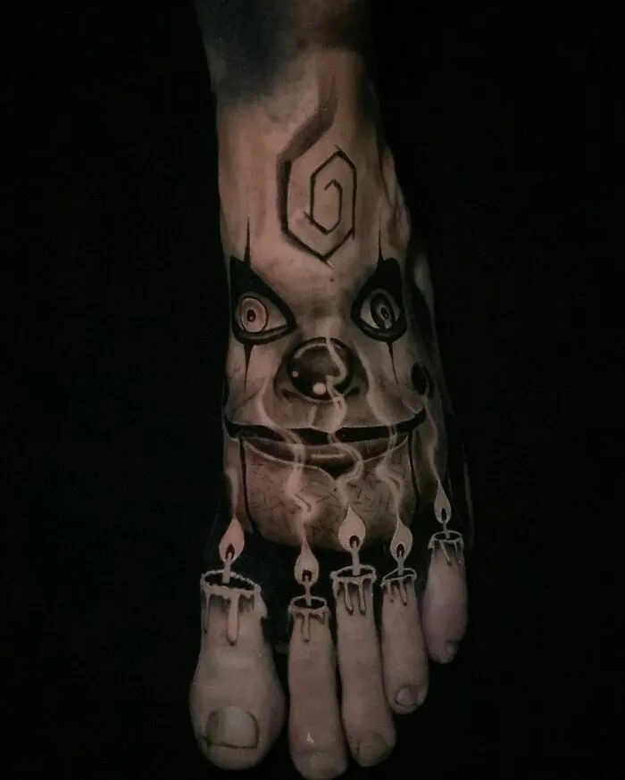 Foot tattoo with realistic detailing of Dead Silence doll face and fingers as candles.