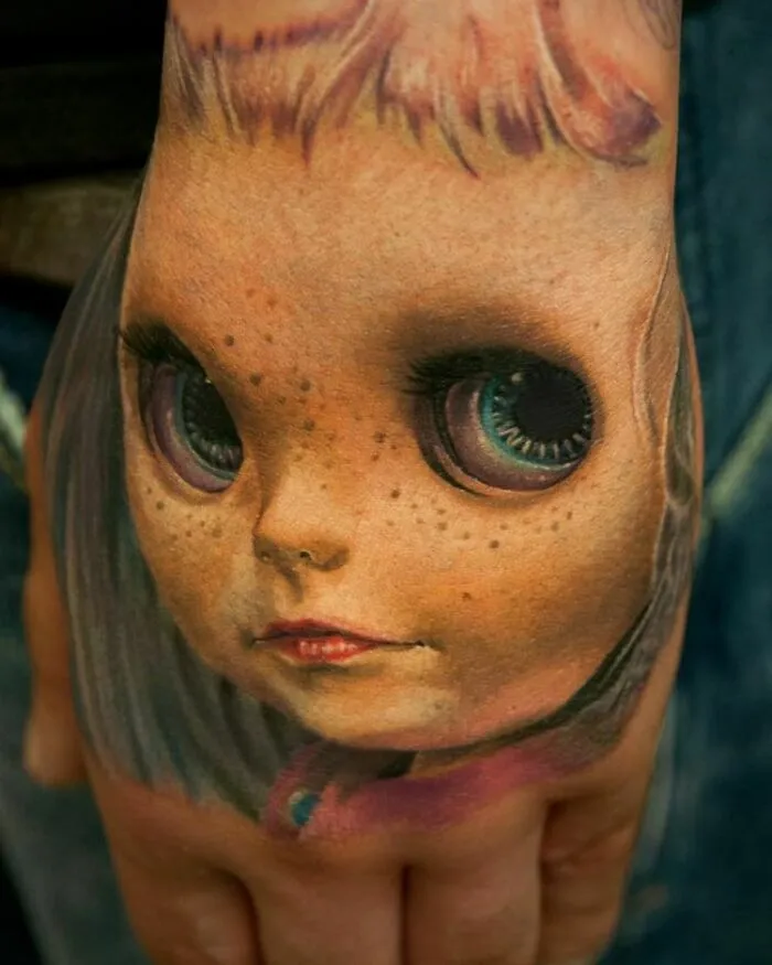 Realistic doll face tattoo on hand showcasing detailed artistry.