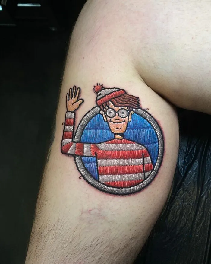 Tattoo of a character with glasses and a red hat, showcasing Eduardo Lozano's unique tattooing style on a person's arm.