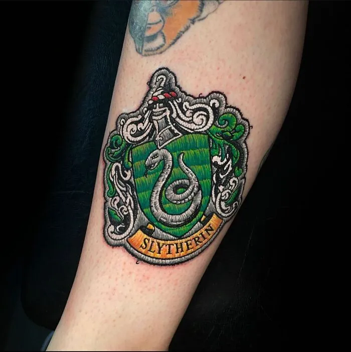 Tattoo of a Slytherin crest on an arm, showcasing a new dimension in tattooing art.
