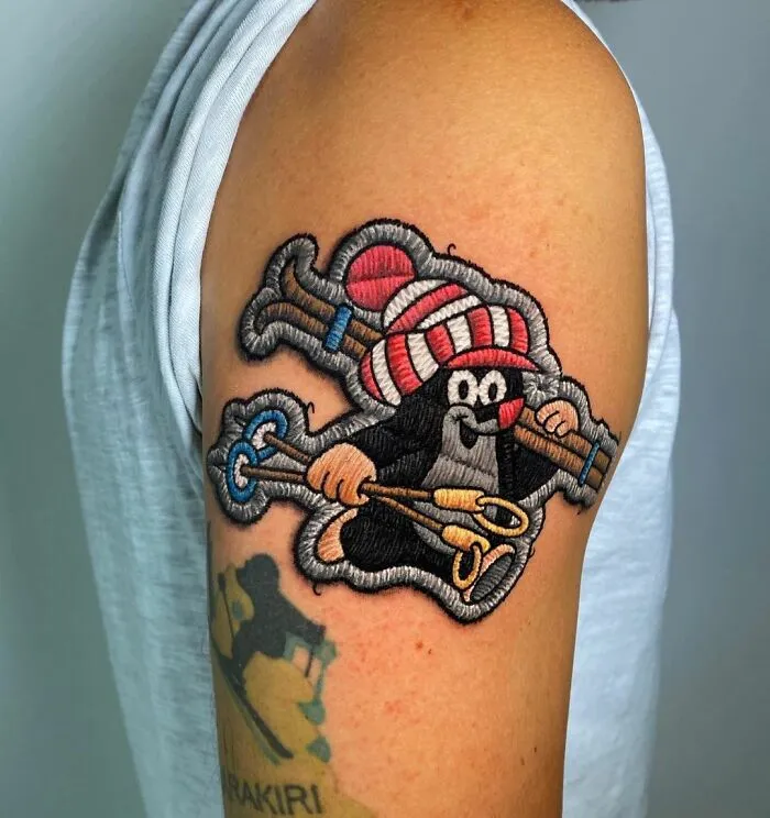 Tattoo showcasing intricate embroidery style by Eduardo Lozano on an upper arm.