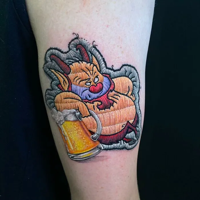 Tattoo by Eduardo Lozano depicting a cartoon character lounging with a beer mug, showcasing unique 3D embroidery style.