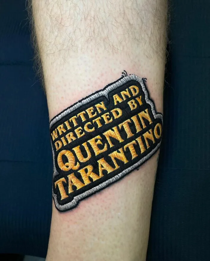 Tattoo on forearm reads "Written and Directed by Quentin Tarantino," showcasing Eduardo Lozano's tattooing style.