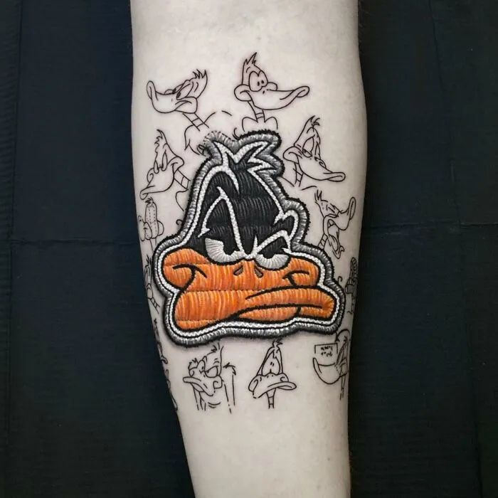 Tattoo by Eduardo Lozano featuring a colorful Daffy Duck design with sketch outlines in the background.