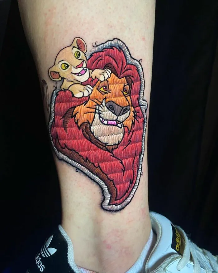 Tattoo of two animated lions by Eduardo Lozano, showcasing innovative embroidery style design on a person's leg.