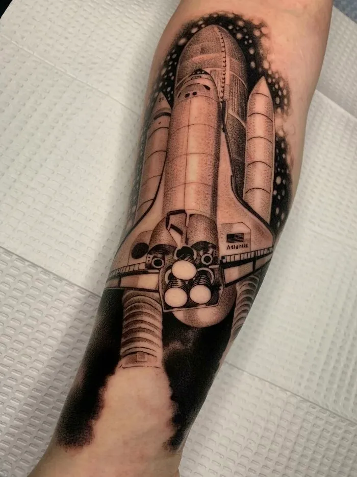 Space tattoo featuring a detailed space shuttle design on arm with starry background.