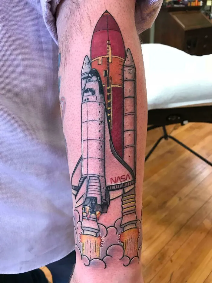 Rocket tattoo on a forearm, showcasing space-themed body art with vibrant colors and detailed design.