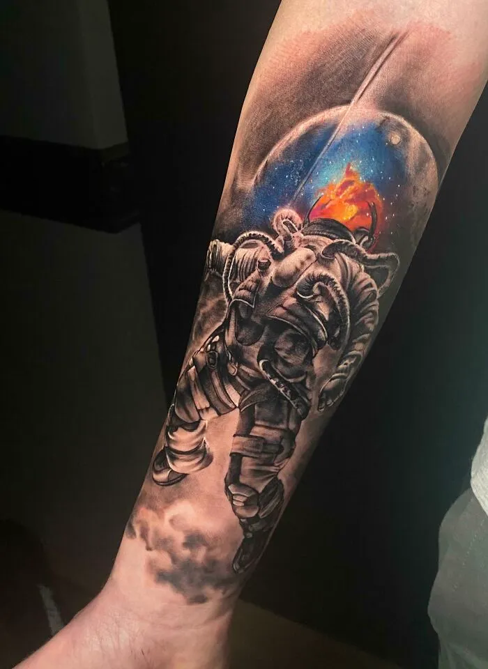 Space tattoo of an astronaut with a fiery galaxy helmet on an arm.