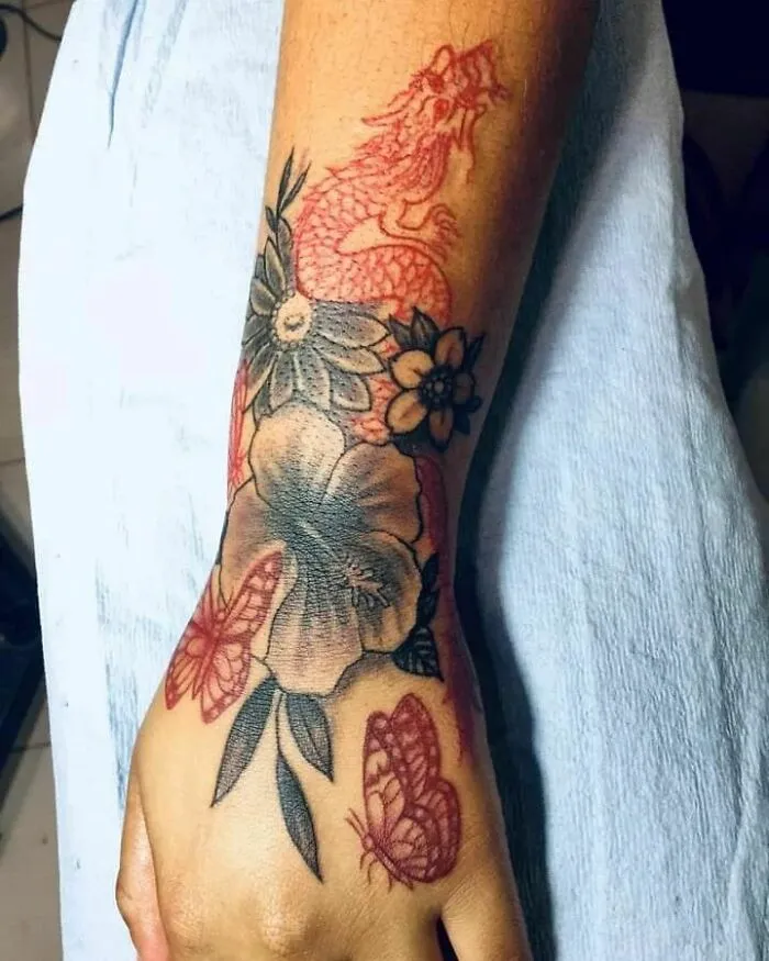 Elegant flower tattoo on hand with dragon and butterfly elements, showcasing artistic beauty and intricate detail.