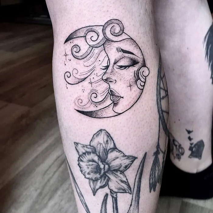 Calf tattoo featuring a stylized moon face and floral design, showcasing cool tattoo art on the leg.