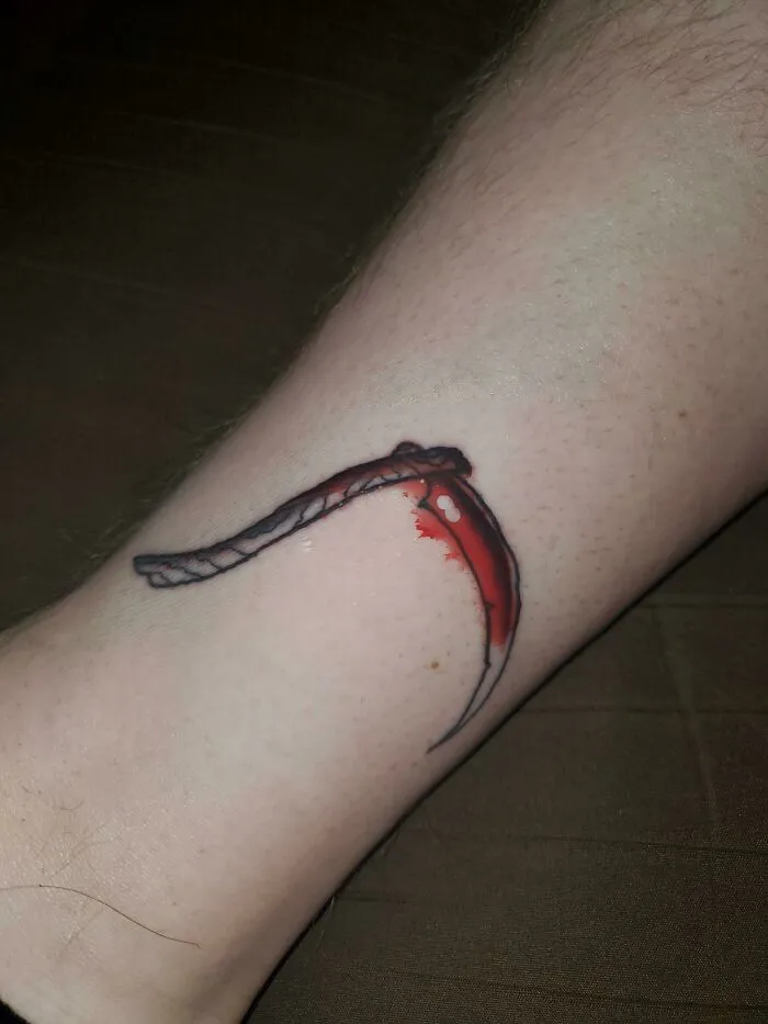 A tattoo of a scythe on a leg, perfectly aligning with a red scar for accidental matching effect.