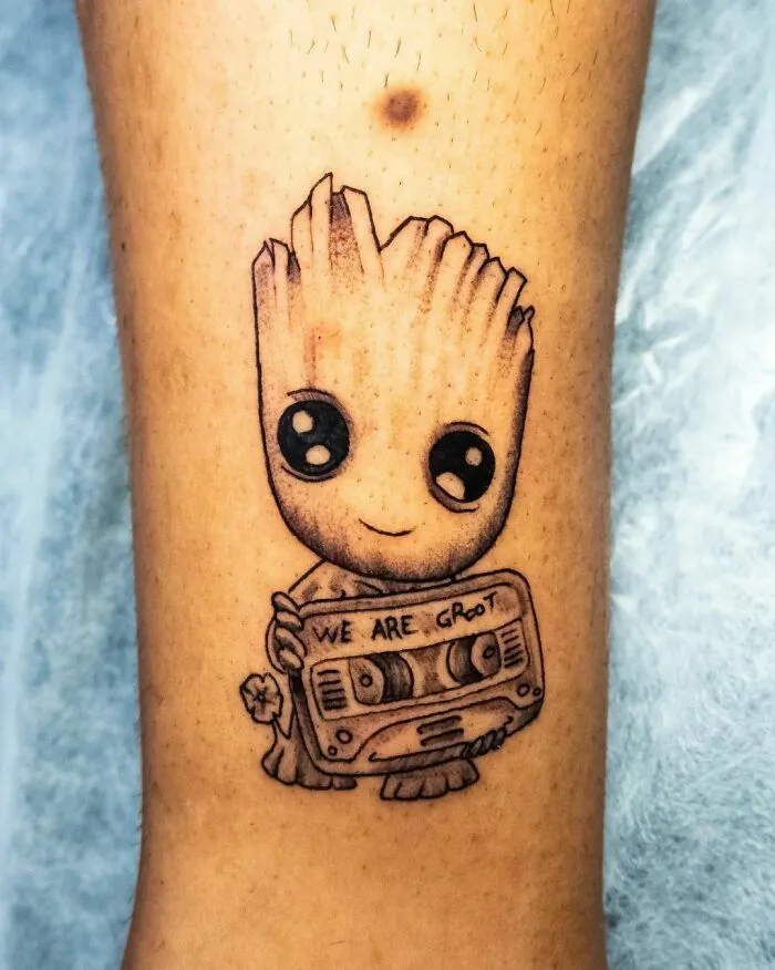 Marvel tattoo of Baby Groot holding a cassette player on a person's arm, showcasing intricate linework and shading.