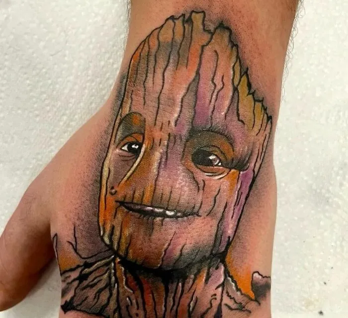 Marvel tattoo of Groot on a hand with detailed wood grain texture and vibrant colors.