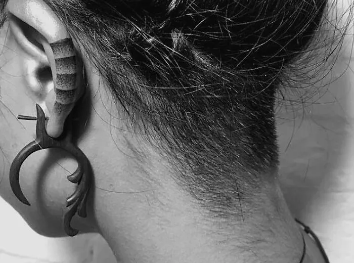 Ear tattoo with intricate design, featuring unique tribal patterns and a wooden earring.