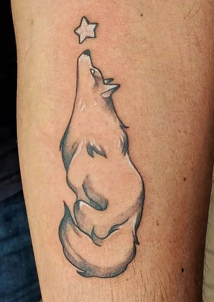 Wolf tattoo looking at a star, highlighting animal kingdom artistry on skin.