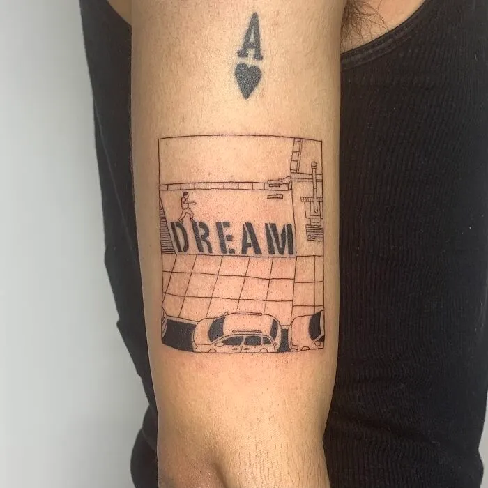 Illustration-style tattoo of a cityscape with the word "Dream" on a person’s arm.