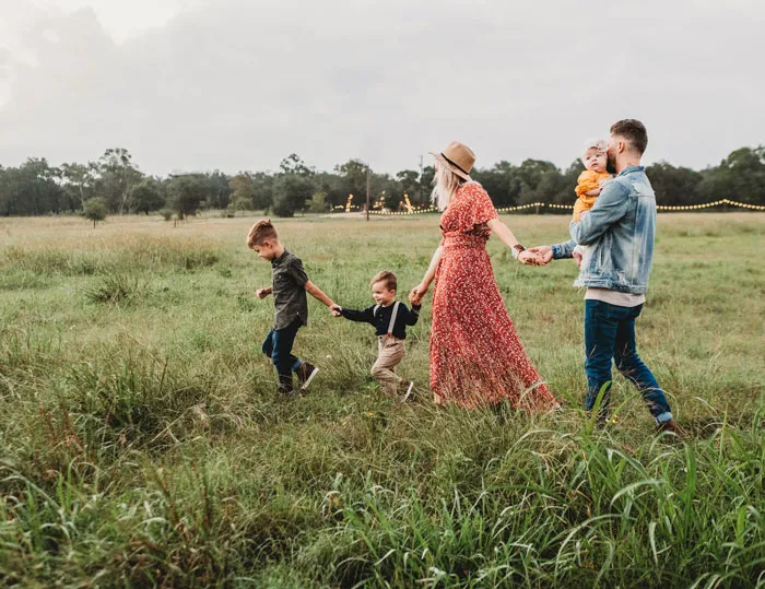 Five-person family is holding hands and walking in the field