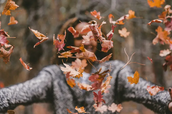 A woman is joyfully throwing autumn leaves in the air