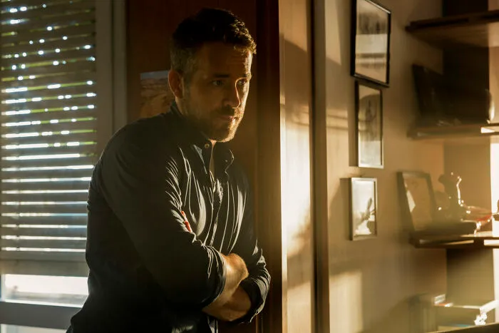 Actor standing thoughtfully in dim light near window blinds, representing one of the highest-paid actors of all time.