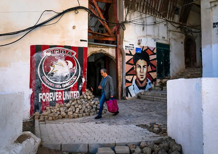 Man Passing Near Murals Of Football And Revolution In The Casbash, North Africa, Algiers, Algeria