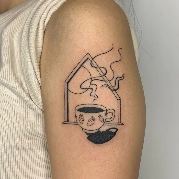 Illustration-style tattoo of a steaming teacup with strawberry design on an arm.