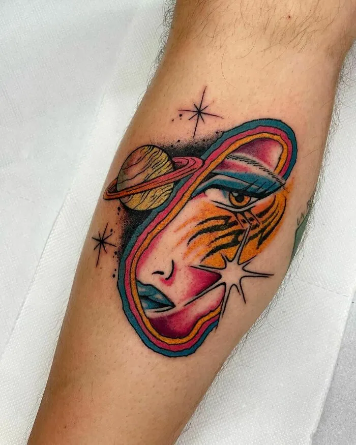 Colorful tattoo featuring astrological elements and a cosmic face design on an arm.