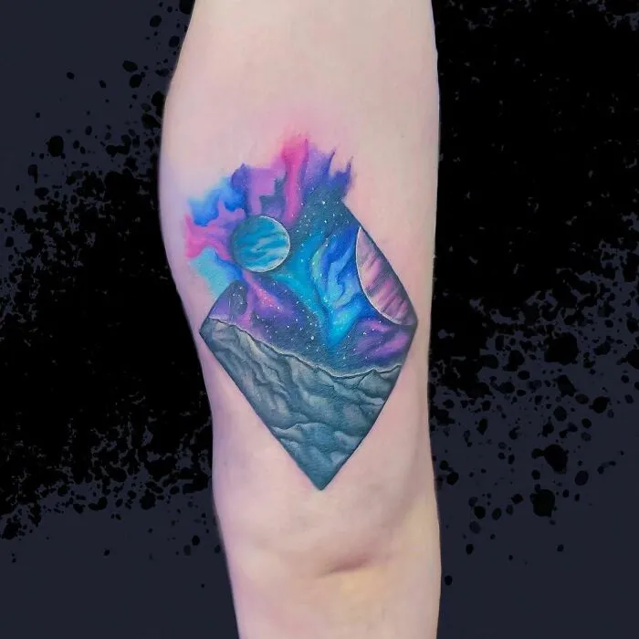 Vibrant outer space tattoo featuring planets and cosmic sky on arm.