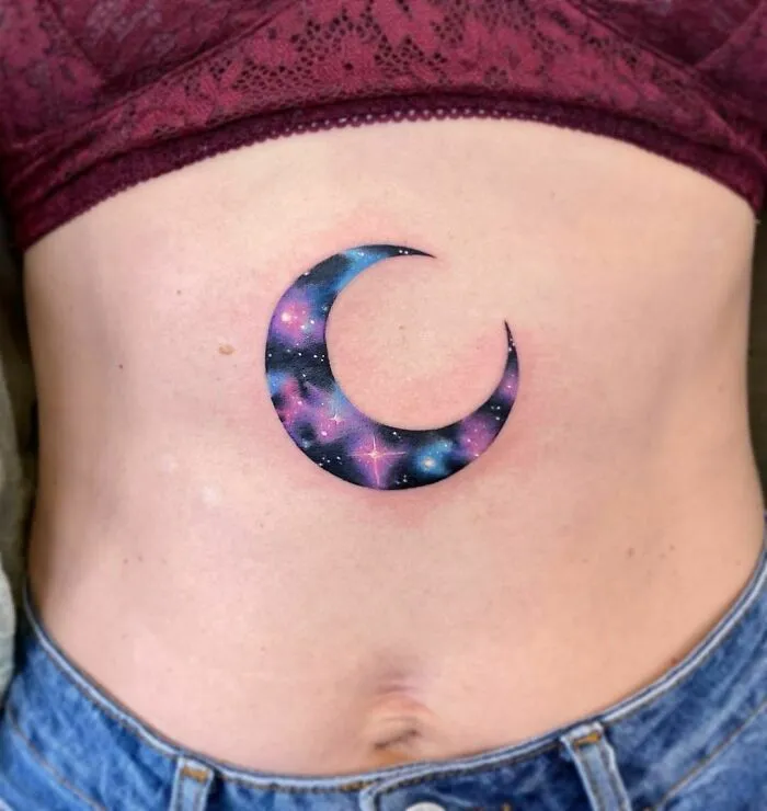 Crescent moon space tattoo with galaxy design on person's torso.