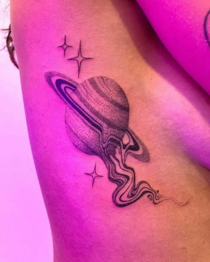 Space tattoo featuring a stylized Saturn with rings and stars on an arm, designed in black ink with a cosmic theme.