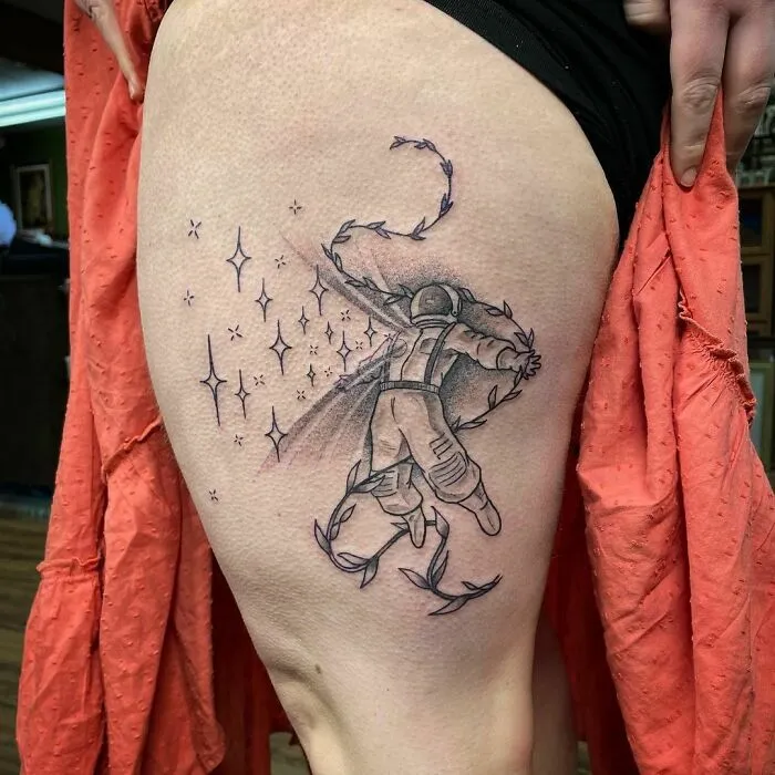 Astronaut space tattoo on thigh, featuring stars and swirling elements, showcasing outer space cool design.