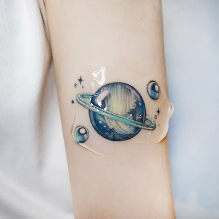 Space tattoo featuring a colorful planet with rings and stars, symbolizing the allure of outer space.