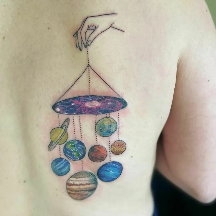 Space tattoo of hand holding planets on skin, featuring colorful cosmic design for astrology fans.