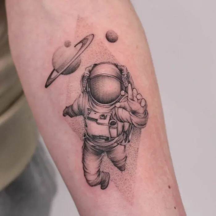 Astronaut tattoo with planets on forearm, perfect for astrology fans.
