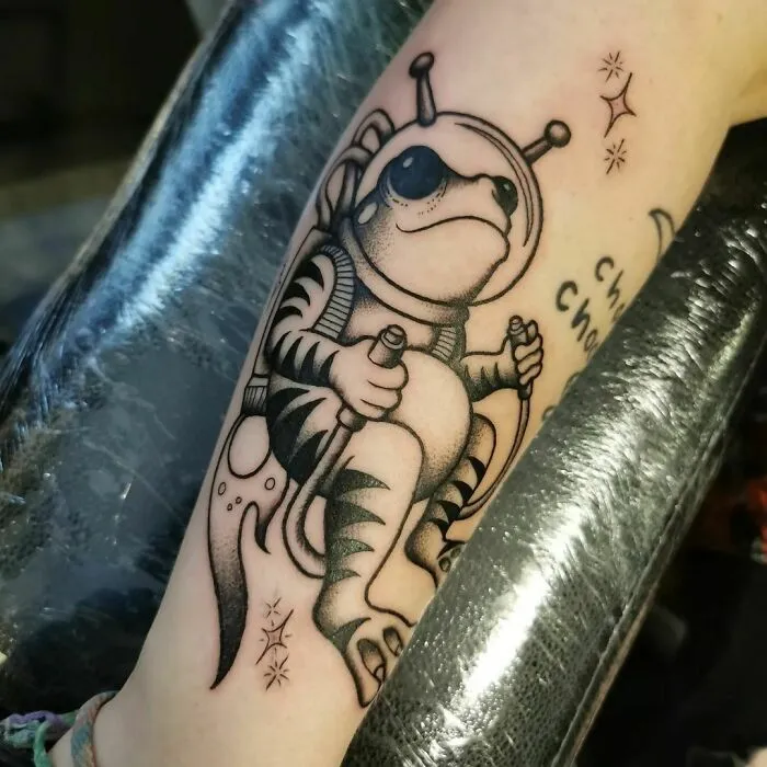 Astronaut frog tattoo design, showcasing creative space-themed art on arm for astrology enthusiasts.