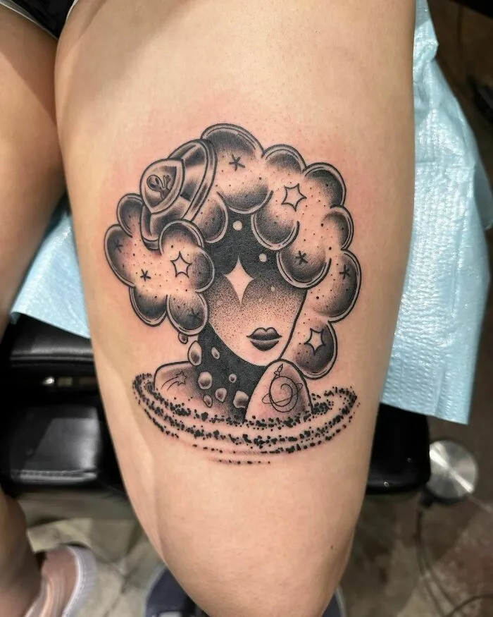 Tattoo of a cosmic woman with curly hair resembling outer space, featuring stars and a planet.