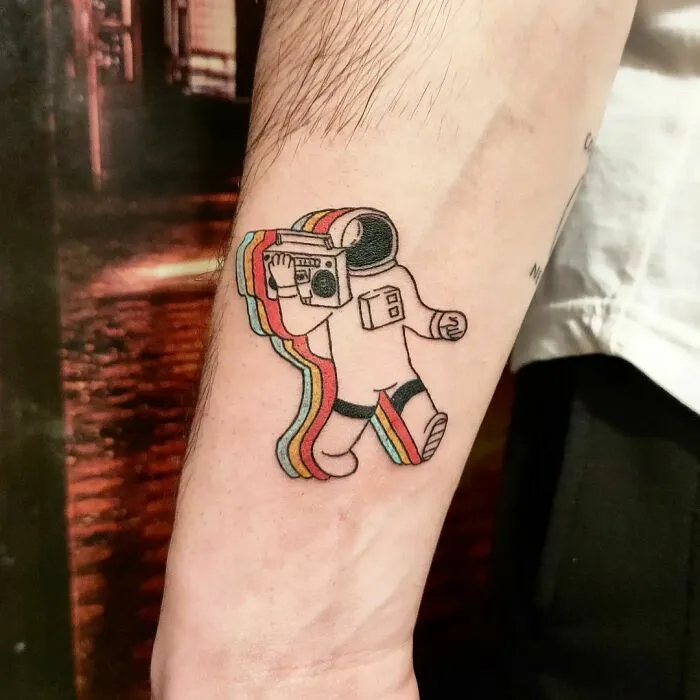 Astronaut tattoo on forearm with rainbow colors, featuring space-themed design.