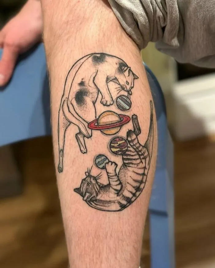 Cat tattoo featuring planets, symbolizing outer space, on a person's leg.