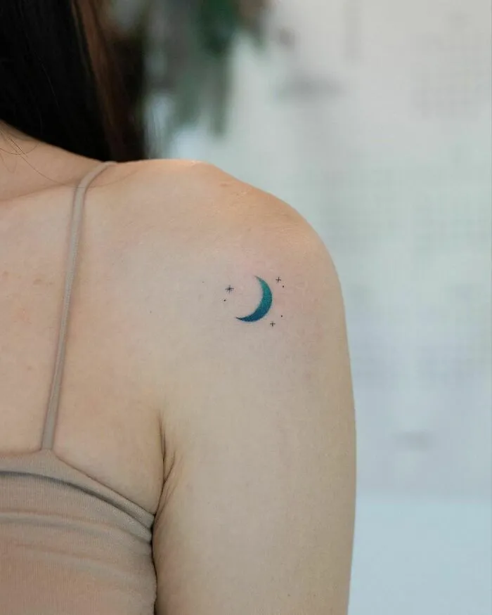 A minimalist crescent moon tattoo with stars on a person's shoulder, perfect for astrology fans and space tattoo enthusiasts.