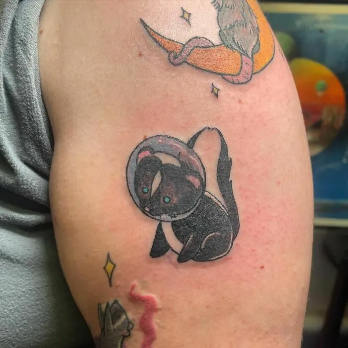 Tattoo of a skunk in a spacesuit on an arm, representing a quirky take on space-themed tattoos.