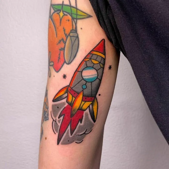 Colorful rocket space tattoo on arm, featuring vibrant planets and stars, capturing the essence of outer space cool.